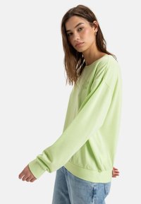 Light green sweatshirt with long sleeves and ribbed cuffs, featuring a logo detail on the chest and a relaxed fit at the hem.