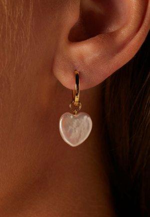 Boucle d'oreille en or avec une goutte de perle iridescente en forme de cœur ; texture lisse et finition brillante ; attachée par une petite anneau en or.