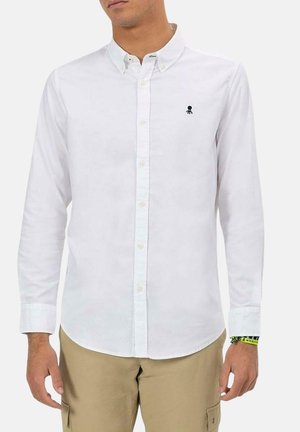 Camisa blanca de manga larga de algodón con un cuello tradicional. Presenta un pequeño logo de un pulpo negro en el lado izquierdo del pecho.