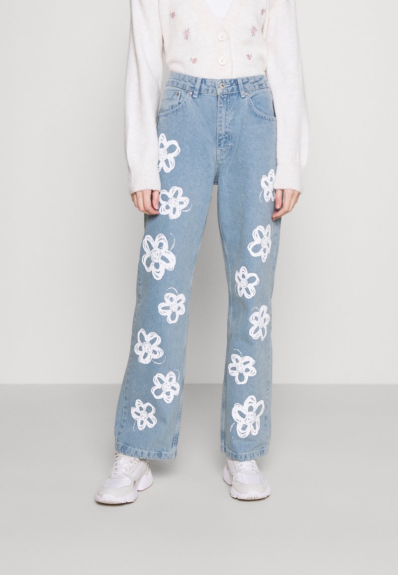 Jeans a gamba larga in denimazzurro chiaro con ricami floreali bianchi sul davanti. Indossati con un cardigan crema chiaro e sneaker bianche.