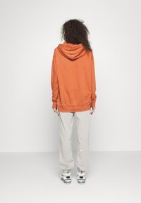 Oranžová mikina s kapucí volného střihu, která je spárována se svetle šedými tepláky. Tento outfit má měkkou látku a ležérní design.