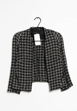Černobílé sako s vzorem houndstooth, střižené do kratší délky a bez límce, s kapsami na zip a visacím štítkem. Texturovaná látka.