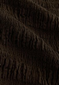 Gros plan sur un tissu texturé marron foncé avec des rainures verticales et un aspect froncé et froissé.