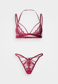 Μπορντό δαντελένιο σουτιέν bralette με κυματιστές άκρες και ρυθμιζόμενους ιμάντες, σε συνδυασμό με τριγωνικό δαντελένιο εσώρουχο με διασταυρούμενες λεπτομέρειες.