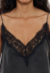 Camiseta negra sin mangas con un escote en V de encaje y patrones florales intrincados, borde de flecos delicados y tirantes ajustables.