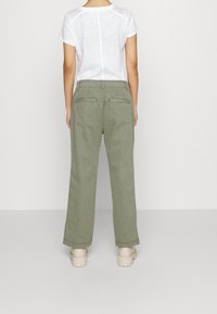 Olivgröna vida byxor med hög midja, utrustade med två bakfickor, kombinerade med en enkel vit t-shirt med kort ärm.