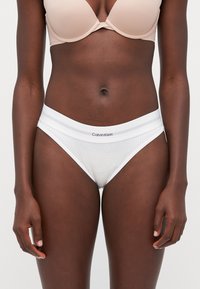 Witte Calvin Klein onderbroeken met een ribbeltextuur, voorzien van een contrasterende elastische tailleband met grijze strepen en logodetails.