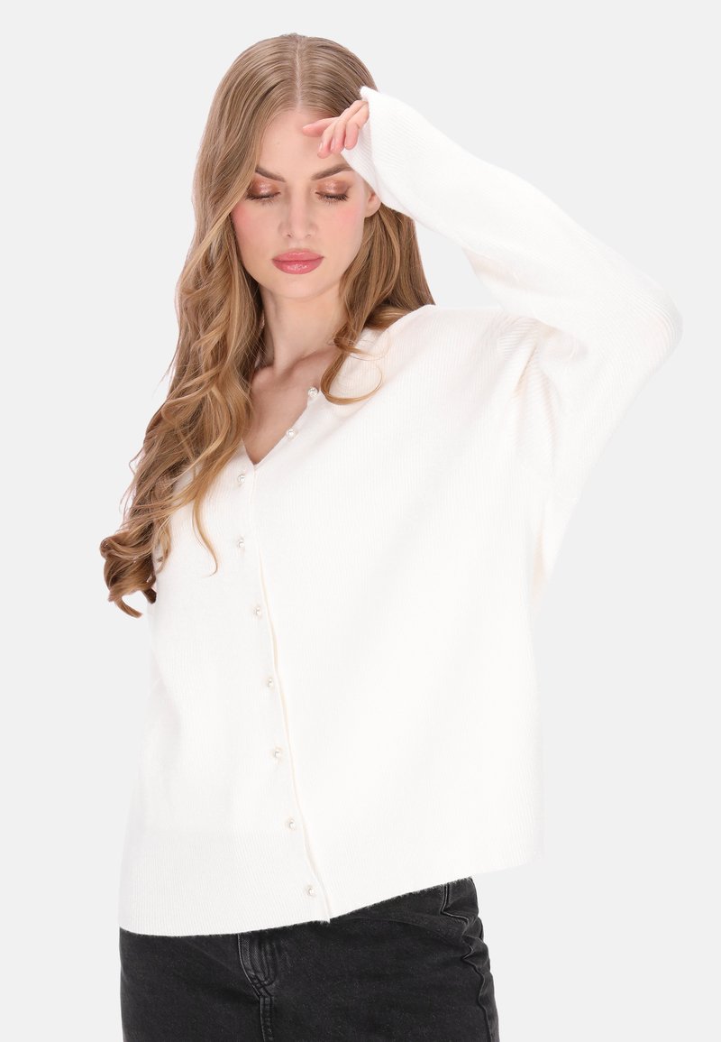 Fehér bordázott kardigán V-nyakkal, gyöngyös gombokkal az elülső részen és hosszú ujjakkal, enyhén túlméretezett szabás.