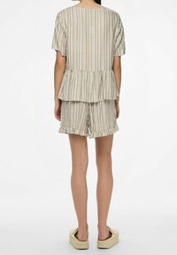 Top peplum a righe di un beige chiaro con maniche corte abbinato a pantaloni corti con orli arricciati e una texture morbida.