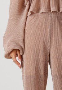 Roze gouden geribbelde breisel loungewear met metallic glans, met uitlopende mouwen en een ontspannen pasvorm. Opvallend textuurpatroon overal.