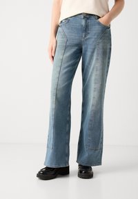 Φαρδιά μπλε τζιν παντελόνια με ξεθωριασμένο φινίρισμα, διαθέτουν μπροστινές τσέπες και χαρακτηριστικές ραφές. Συνδυασμένα με χοντρές μαύρες μπότες με πλατφόρμα.