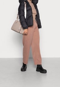 Czarna puchowa kurtka, ryflowy beżowy sweter, jasnoróżowe spodnie typu wide-leg oraz czarne botki na grubej pięcie. Nosi beżową torebkę.