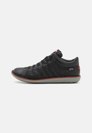 Black leather sneaker with elastic laces, textured upper, and grey rubber sole. Features red accents and logo on heel.