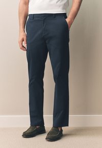 Chinos en coton bleu marine avec une coupe droite, dotés de poches latérales et d'un devant plat, associés à des chaussures à enfiler vert foncé.