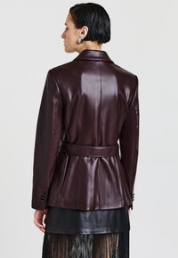 Bordeauxfarbene Lederjacke mit taillierter Form, tailliertem Bund und Reverskragen. Verfügt über Nähte und Knopfakzente an den Ärmeln.