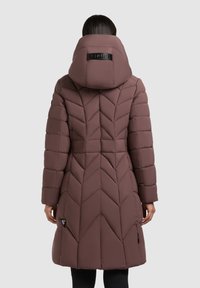 Barna puffernadrág, chevron tűzéssel, magas gallérral és állítható kapucnival, valamint cipzáras oldalsó zsebekkel. Simogató, párnázott textúra.