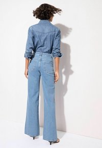 Hellblaues Denim-Hemd und weit geschnittene Jeans mit lässigem Schnitt. Das Hemd hat hochgerollte Ärmel und die Jeans verfügen über zwei Gesäßtaschen.