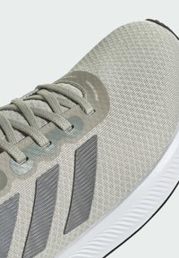 Svetlošedé bežecké tenisky s textúrovaným zvrškom, s sivými pruhmi, plochými šnúrkami a bielou gumovou podrážkou s výrazným vzorom.