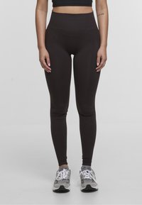 Leggings marroni a vita alta realizzati in un tessuto elasticizzato con una superficie liscia, abbinati a scarpe sportive grigie con lacci bianchi.