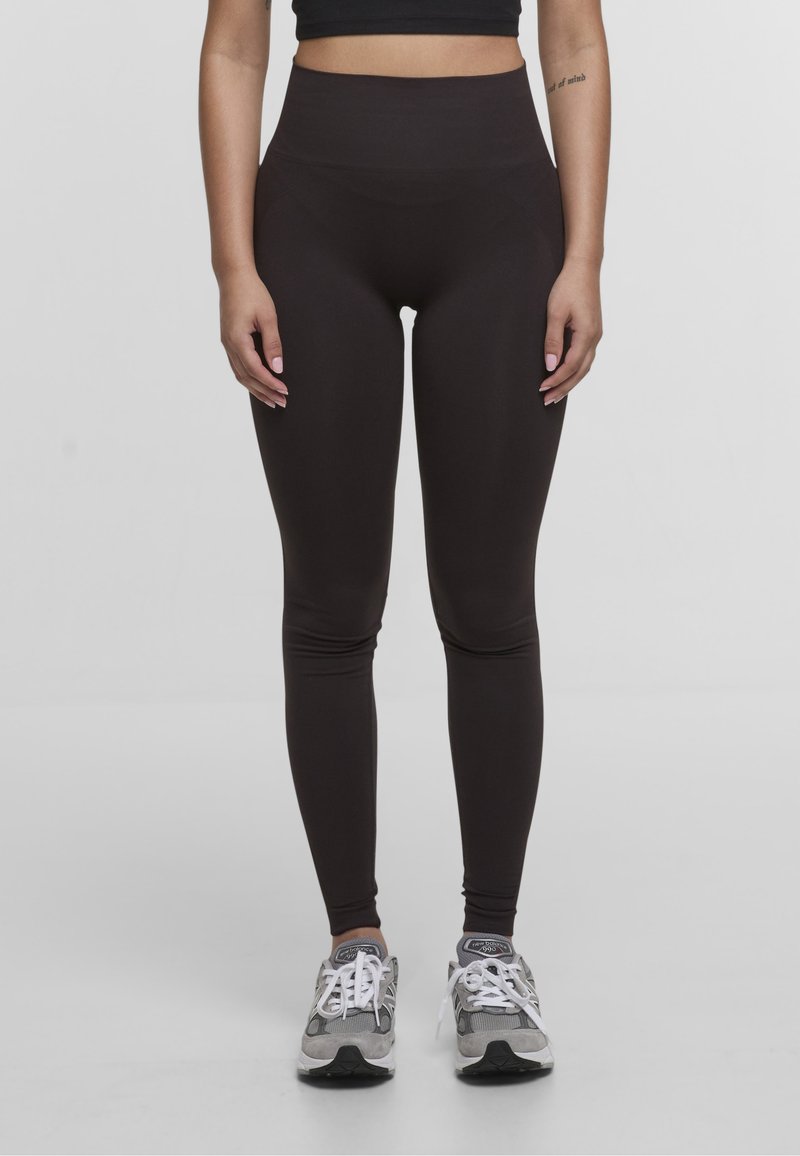 Leggings marroni a vita alta realizzati in un tessuto elasticizzato con una superficie liscia, abbinati a scarpe sportive grigie con lacci bianchi.