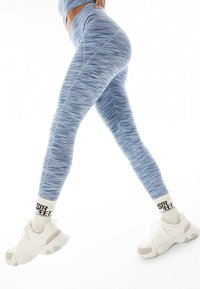 Blå, texturerade leggings med ett subtilt randigt mönster, hög midja, i kombination med vita sneakers och ankelsockor med text.