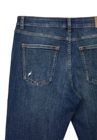 Jeans en denim bleu foncé avec une poche arrière légèrement usée, ornée de surpiqûres orange. Le tissu a une texture lisse et un poids moyen.