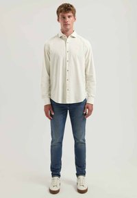 Helebeige nööbiga särk pikkade varrukatega, koos tumehallide teksade ja valgete tossudega. Minimalistlik disain ja pehme tekstuur.