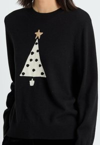 Pull noir en tissu doux, orné d'un motif d'arbre de Noël blanc avec des pois noirs et une étoile dorée au sommet.