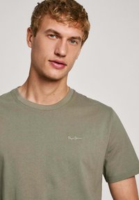 T-shirt in cotone verde oliva con colletto rotondo e maniche corte, con logo "Pepe Jeans" ricamato sul lato sinistro del petto.