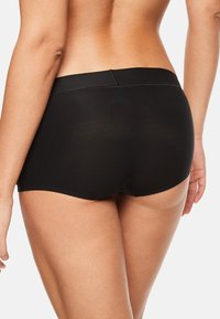 Shorts noirs sans couture pour garçons avec une ceinture douce et élastique et une couverture minimale, présentant une texture de tissu douce et extensible.