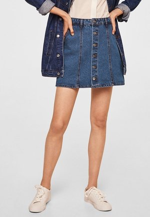 Gonna in denim con vita alta, chiusura frontale con bottoni, dettagli di cucitura leggeri e una forma ad A che esalta la figura. Abbinata a sneakers bianche.