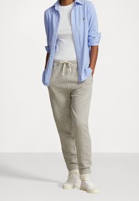 Ljusblå knapp-up skjorta, vit t-shirt under, grå träningsbyxor med snöre, och vita sneakers med texturerade detaljer.