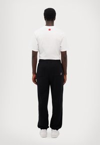 White cotton t-shirt with a red graphic on the back, paired with black sweatpants featuring two rear pockets and an embroidered logo.
