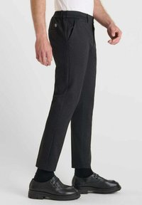Zwarte op maat gemaakte broek met zakken, slim fit ontwerp, gestructureerde stof en een zichtbaar logo op de achterzak. Gdragend met zwarte formele schoenen.