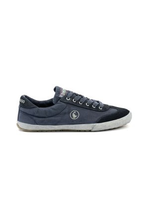 Zapatilla baja de lona de color gris oscuro con suela de goma blanca, puntera negra, cierre de cordones y logo circular en el lateral.