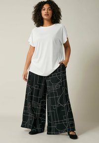 Camicia bianca a maniche corte con dettagli testurizzati sulle spalle, abbinata a pantaloni neri a gamba larga con un motivo geometrico di linee bianche.