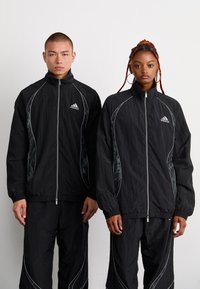 Vestes zippées noires avec des accents argentés contrastants et des motifs sur les côtés, accompagnées de pantalons assortis ; fabriquées en tissu léger.