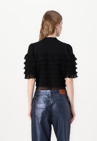 Top corto nero con dettagli a frange stratificate sulle maniche. Abbinato a un paio di jeans blu navy lucidi a vita alta con due tasche posteriori.
