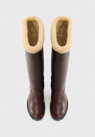 Brown leather knee-high boots with a textured finish and a fluffy beige lining at the opening. Thick black rubber soles for traction.