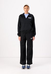 Svart fleece sweatshirt med kvart glidelås og kengurulomme, sammen med matchende joggebukser. Har "New Balance"-logo i hvitt.