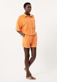 Oranje badstof tweedelige set met een kortarm overhemd met knoopsluiting en zak, en bijpassende shorts met witte accenten.