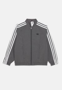 Šedá tréningová bunda Adidas s bielymi trojfarebnými pruhmi na rukávoch, predným zipsom, elastickými manžetami a logom Adidas na ľavej hrudi.