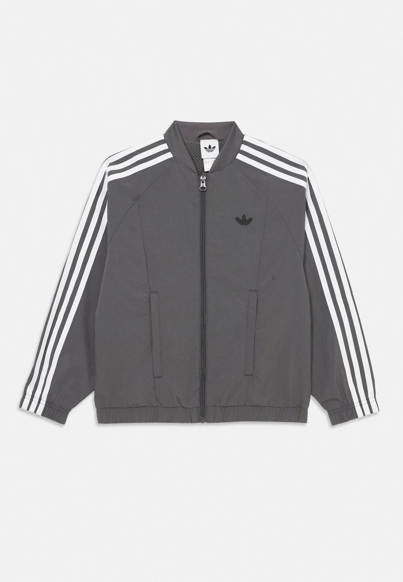Šedá tréningová bunda Adidas s bielymi trojfarebnými pruhmi na rukávoch, predným zipsom, elastickými manžetami a logom Adidas na ľavej hrudi.