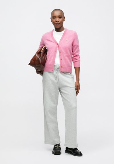 Cardigan din lână roz cu nasturi, asociat cu un tricou alb și pantaloni de trening gri. Accesoriile includ o geantă din piele maro și pantofi negri.