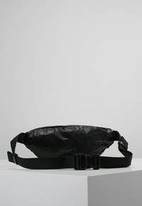 Czarna saszetka na talię wykonana z błyszczącego materiału, o zaokrąglonym kształcie, z regulowanym paskiem i bezpiecznym plastikowym zapięciem.