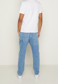 Ljust blå denimjeans med en avkopplad passform, med bakfickor och lätt blekning. Matchas med en enkel vit t-shirt med kort ärm.