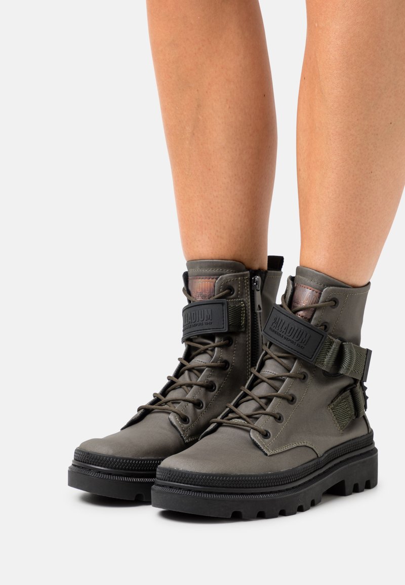 Botas de tobillo verde oliva hechas de material duradero, con cordones, una correa y una suela de goma texturizada con surcos profundos para mayor tracción.