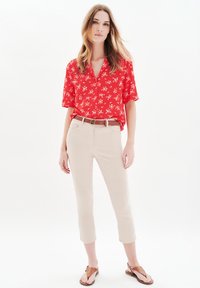 Röd blommig kortärmad skjorta matchad med ljusbeige kapade byxor; ett brunt bälte och bruna sandaler fulländar looken. Släta texturer.