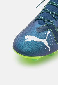 Scarpa da calcio blu con texture, suola e lacci verde neon, con logo Puma bianco nell'area della punta.