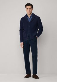 Cardigan ribbed blu navy con colletto a scialle, tasche anteriori e chiusura a bottoni, abbinato a chinos blu navy e scarpe marroni.